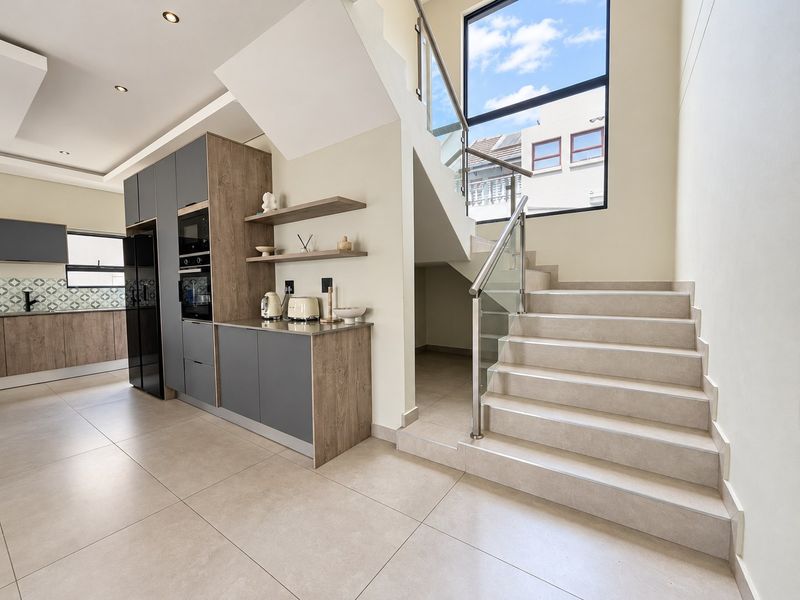 Modern open-plan kitchen area featuring sleek cabinetry, built-in appliances, and a contemporary staircase with glass balustrades, illuminated by a large feature window.