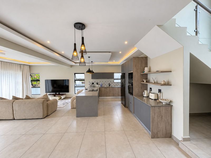 Modern open-plan living area featuring a sleek kitchen with integrated appliances, a central island, and a staircase with a glass balustrade.