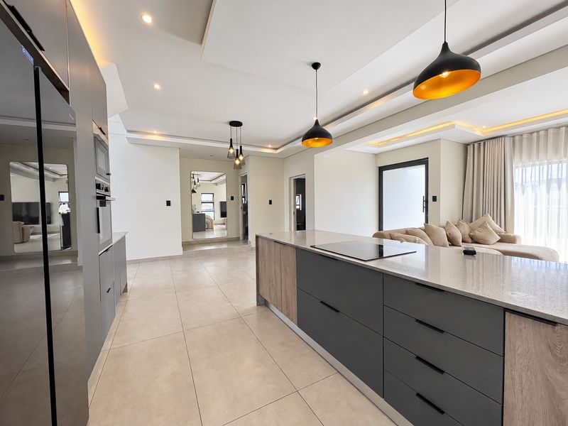 Modern open-plan kitchen featuring a large island with stone countertops, integrated appliances, and stylish pendant lighting, seamlessly flowing into the living area.