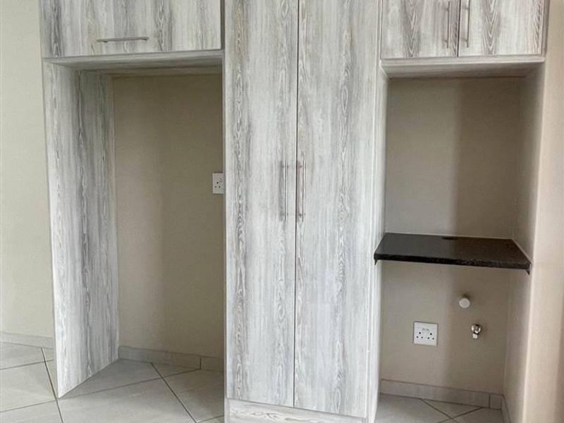 A clean, modern kitchen area featuring light wood-look built-in cabinetry, granite counter space, and tiled flooring with dedicated appliance and plumbing connections.