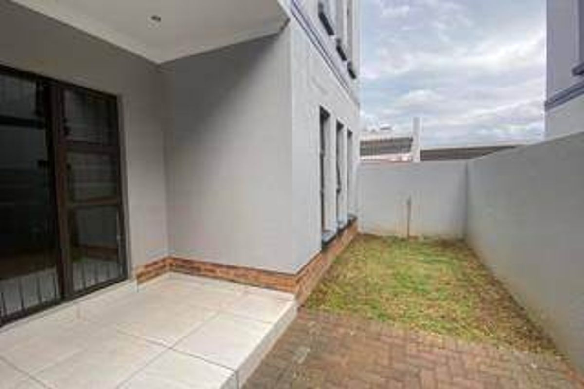 A private rear courtyard featuring a tiled patio, paved section, and a small lawn area, enclosed by a boundary wall.
