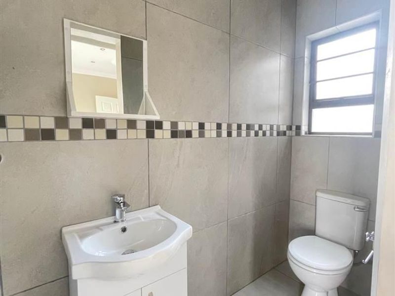 A clean, modern bathroom featuring neutral grey wall and floor tiles, a white vanity cabinet with basin, and a functional toilet.