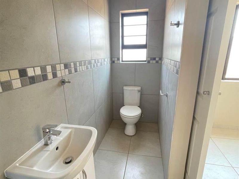 A clean, functional bathroom featuring neutral wall and floor tiles, a modern vanity unit with a basin, and a standard toilet.
