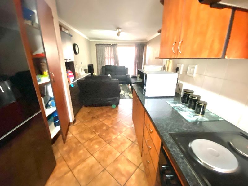 Open-plan kitchen and living area featuring tiled flooring, wooden cabinetry, and an electric hob, offering a functional layout for daily living.