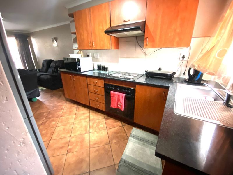 Open plan kitchen featuring wooden cabinetry, dark countertops, and tiled flooring, seamlessly flowing into the adjacent living area.