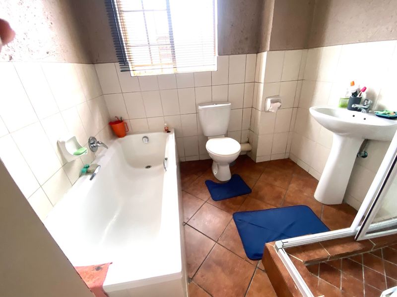 A functional bathroom featuring a bathtub, pedestal basin, and toilet with tiled flooring and wall finishes, requiring minor cosmetic updates.