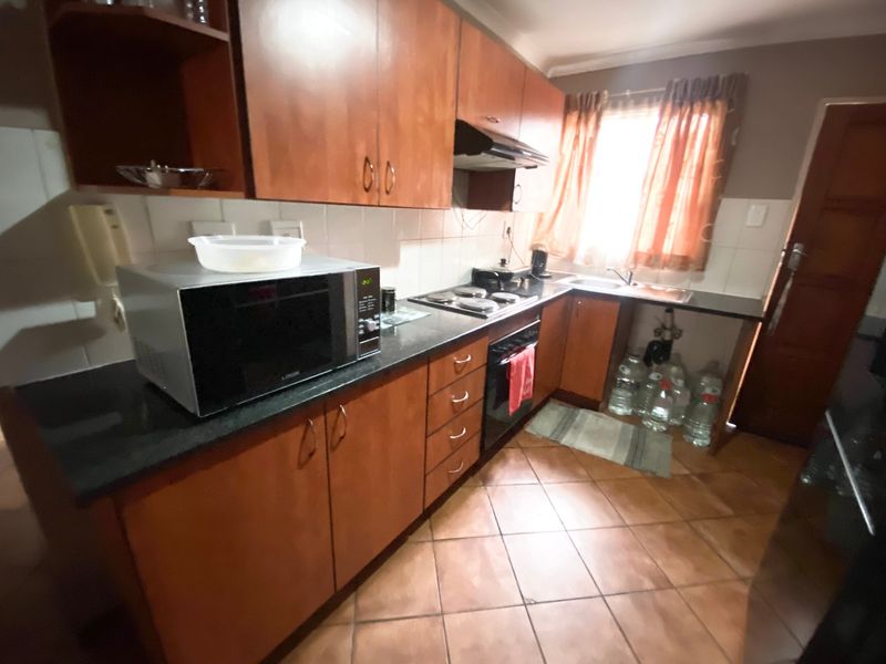 A functional kitchen featuring wooden cabinetry, black granite countertops, an electric hob, and an integrated oven, offering a practical layout for daily meal preparation.