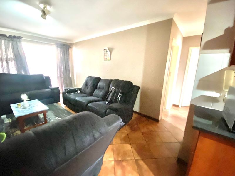 A living room area featuring tiled flooring and coved ceilings, providing a functional space with access to adjacent rooms.