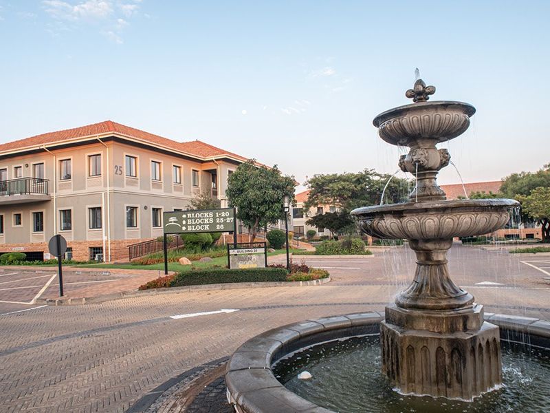 A well-maintained commercial office complex featuring a decorative stone fountain, paved driveway, and clear directional signage for multiple building blocks.