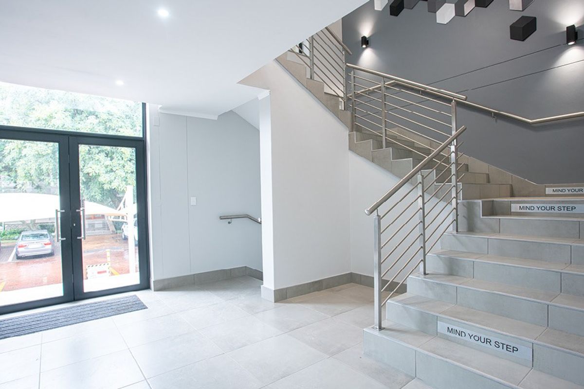 Modern commercial entrance lobby featuring tiled flooring, a prominent staircase with stainless steel railings, and large glass double doors providing natural light.