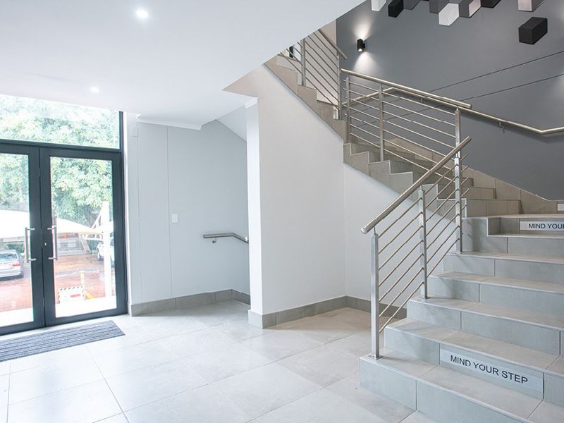 Modern commercial entrance lobby featuring tiled flooring, a prominent staircase with stainless steel railings, and large glass double doors providing natural light.