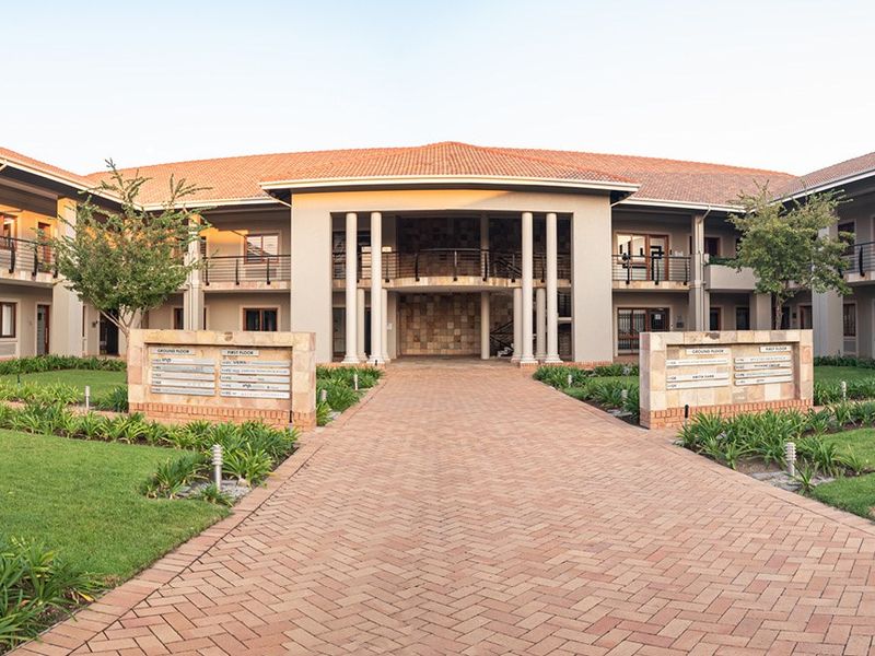 A professional exterior view of a commercial office complex featuring a central paved walkway, stone signage pillars, and well-maintained landscaped gardens.