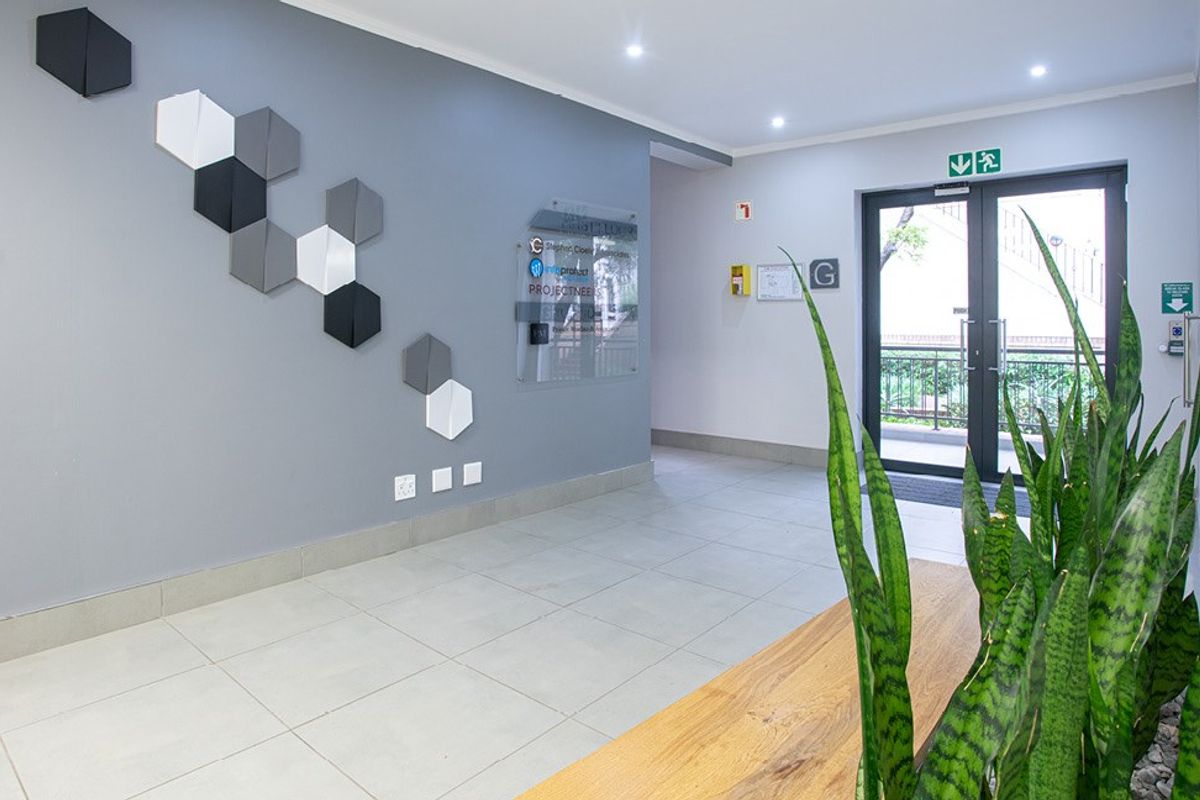 A clean and professional commercial building entrance lobby featuring tiled flooring, recessed lighting, and glass double doors leading to the exterior.