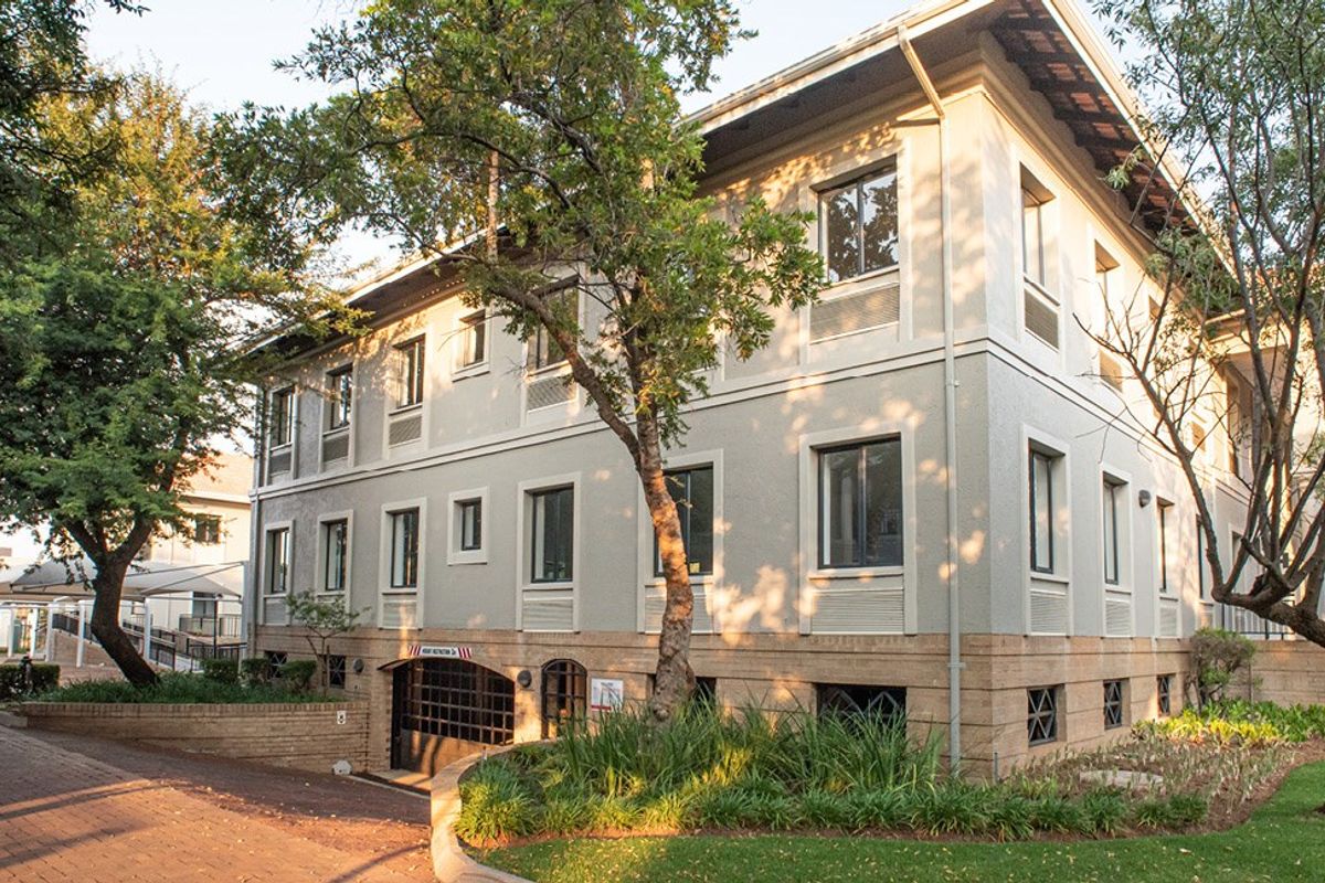 A well-maintained multi-story commercial building featuring a stucco facade, brick base, and secure underground parking access, surrounded by mature trees and landscaped grounds.