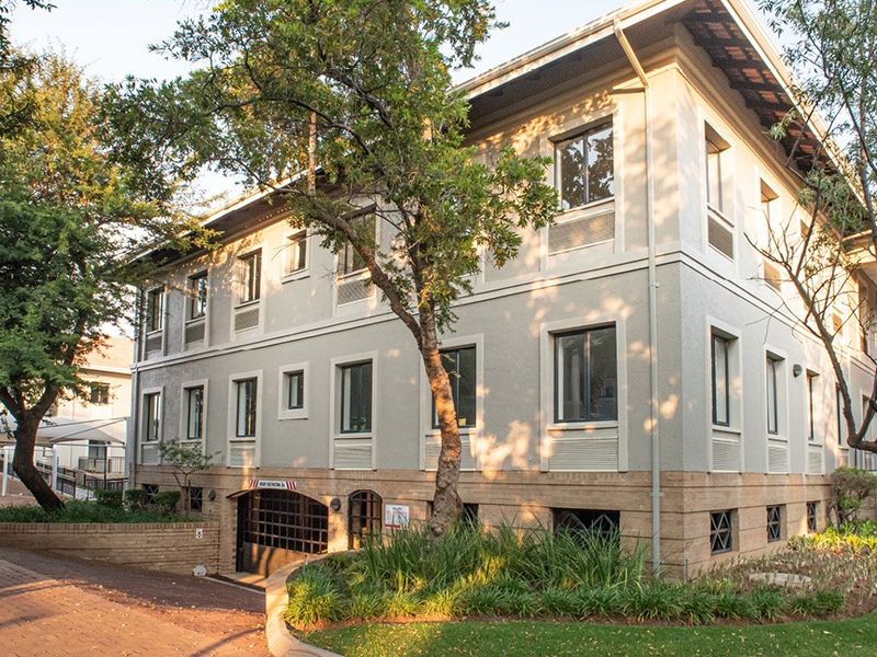 A well-maintained multi-story commercial building featuring a stucco facade, brick base, and secure underground parking access, surrounded by mature trees and landscaped grounds.