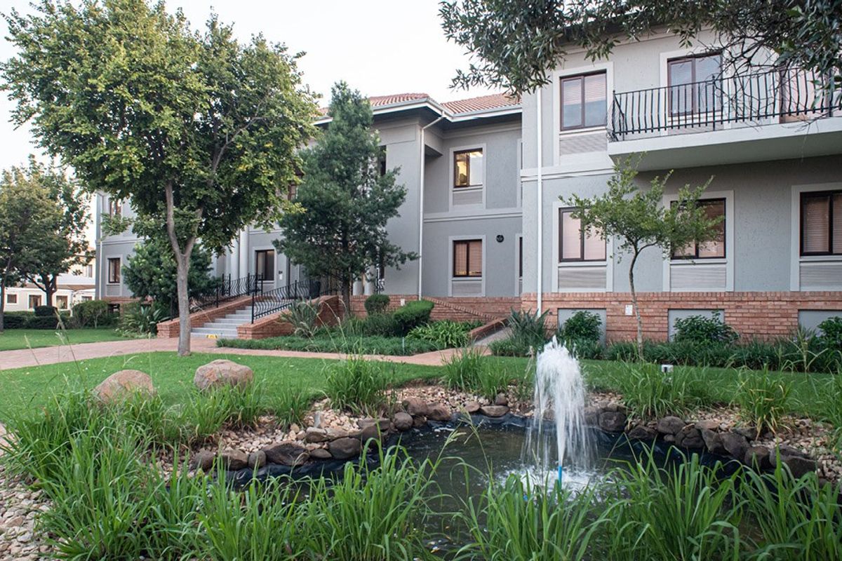 A well-maintained commercial building exterior featuring a landscaped garden, a decorative water fountain, and paved walkways leading to the building entrance.