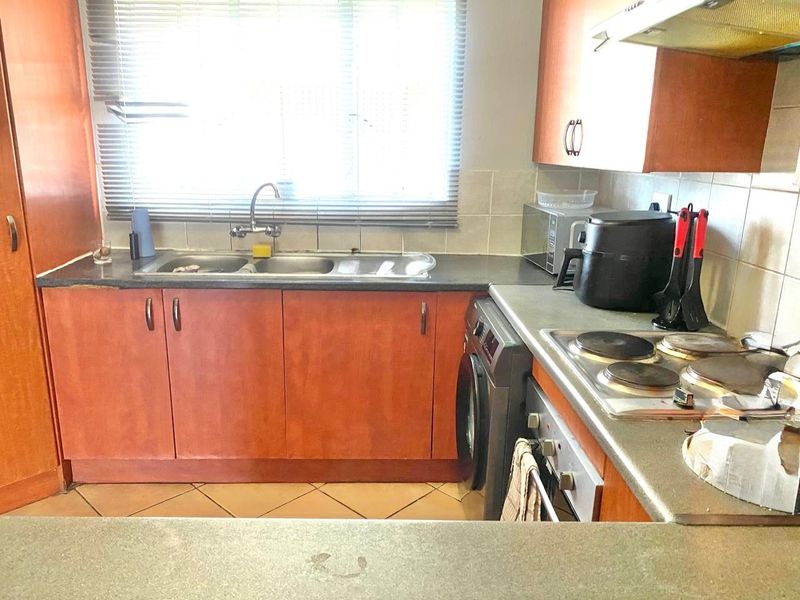 Functional kitchen featuring laminate cabinetry, double bowl sink, built-in oven, electric hob, and tiled backsplash with ample counter space.