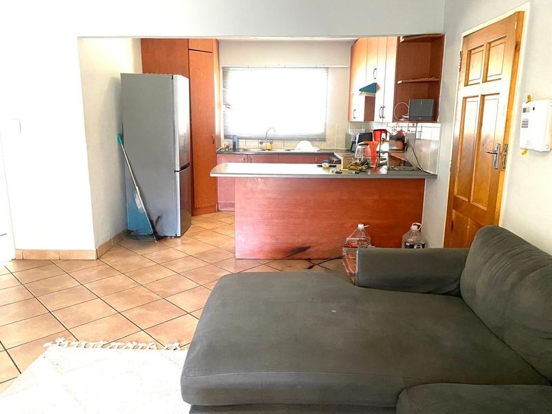Open plan kitchen and living area featuring tiled flooring, wooden cabinetry, and a breakfast bar counter, offering a functional layout for daily living.