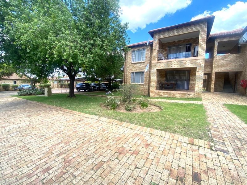 Exterior view of a face brick apartment complex featuring paved driveways, landscaped garden areas, and private balconies with security gates.
