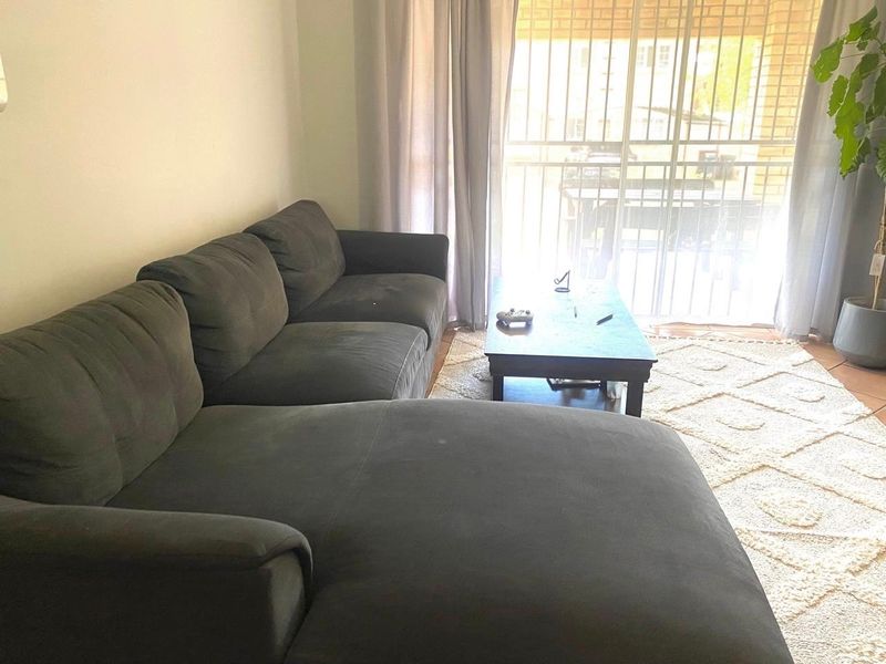 A comfortable living room featuring tiled flooring and a large sliding glass door with a security gate, providing access to the outdoor area.