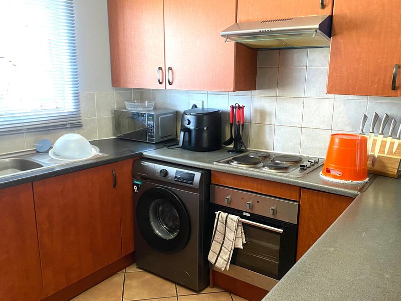 Functional kitchen featuring laminate cabinetry, built-in oven, electric hob, extractor fan, and tiled backsplash with integrated laundry appliance space.