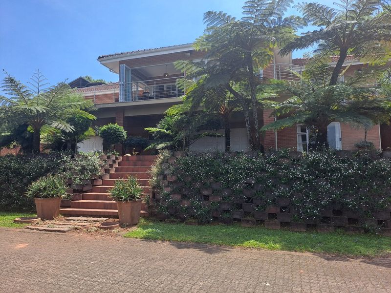A multi-level brick house featuring a paved driveway, landscaped retaining wall, and an elevated balcony with metal railings.