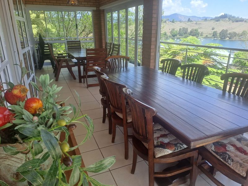 A spacious covered patio featuring tiled flooring, brick pillars, and glass sliding doors, offering scenic views of the surrounding landscape and water.