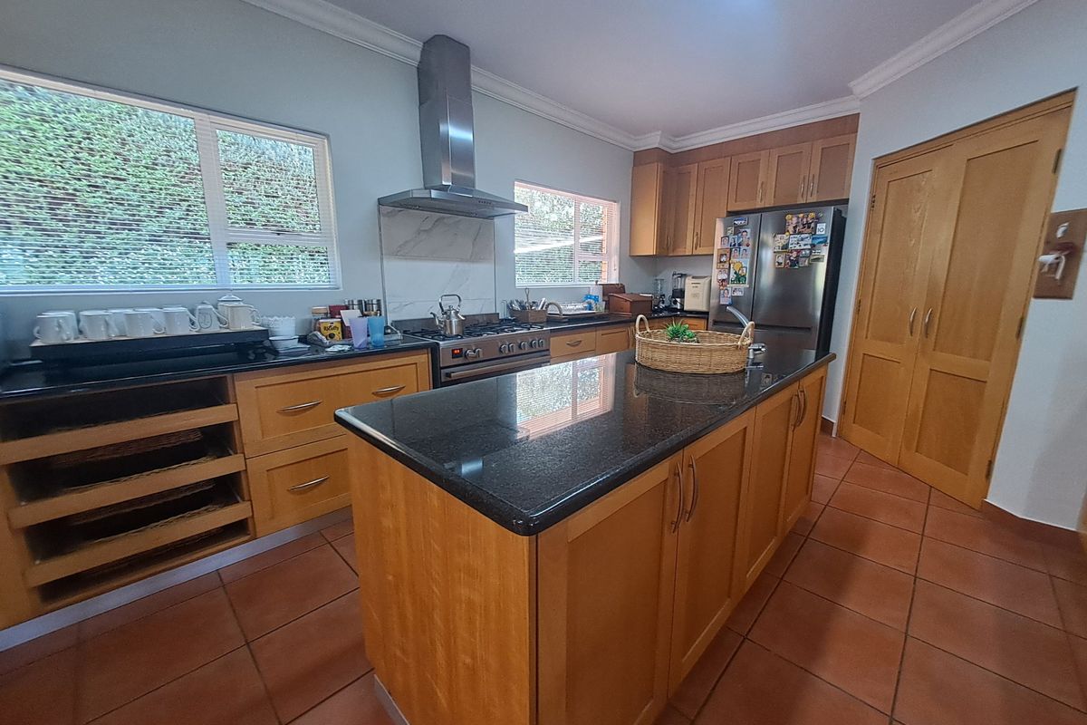 A well-appointed kitchen featuring wooden cabinetry, granite countertops, a central island, and a stainless steel gas stove with an extractor fan.