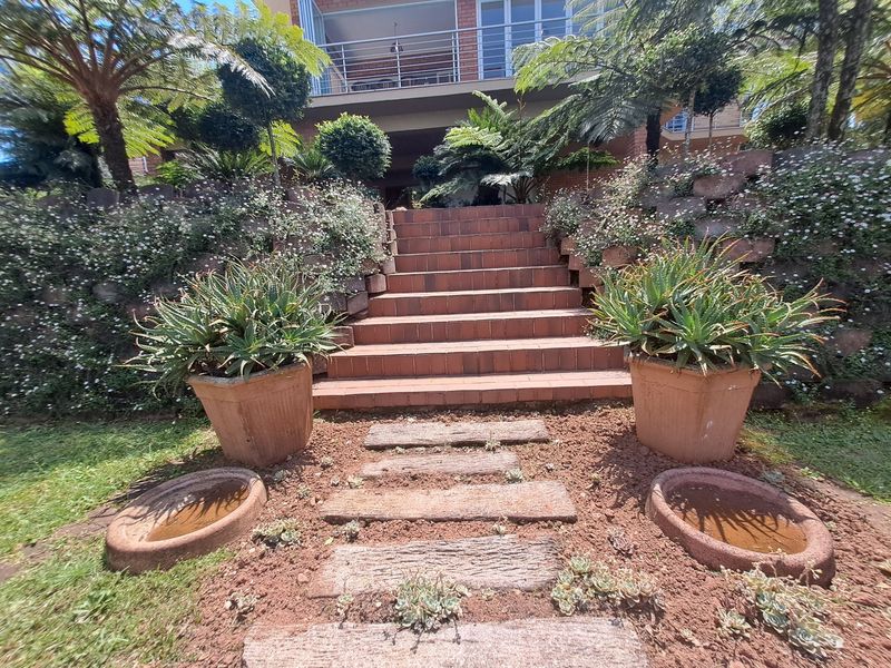 A landscaped rear garden featuring a brick staircase leading up to a balcony with metal railings.