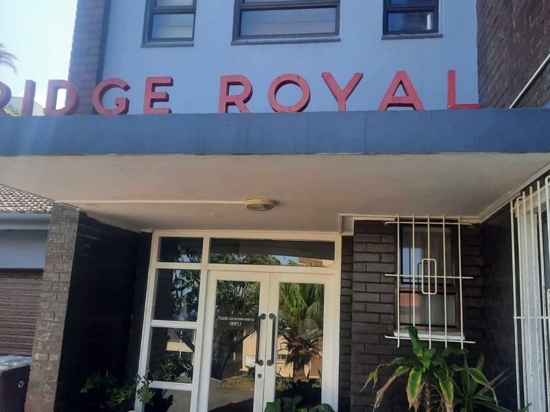 The front entrance of the Ridge Royal apartment complex, featuring a brick facade, protective canopy, and secure glass door access.