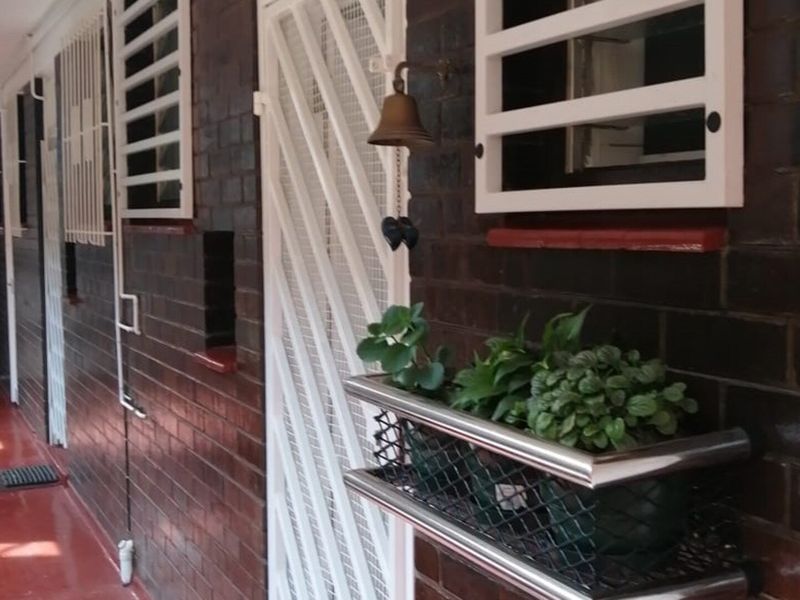 An exterior-facing apartment hallway featuring dark brick walls, white security gates, and window bars, providing a secure and functional transition space.
