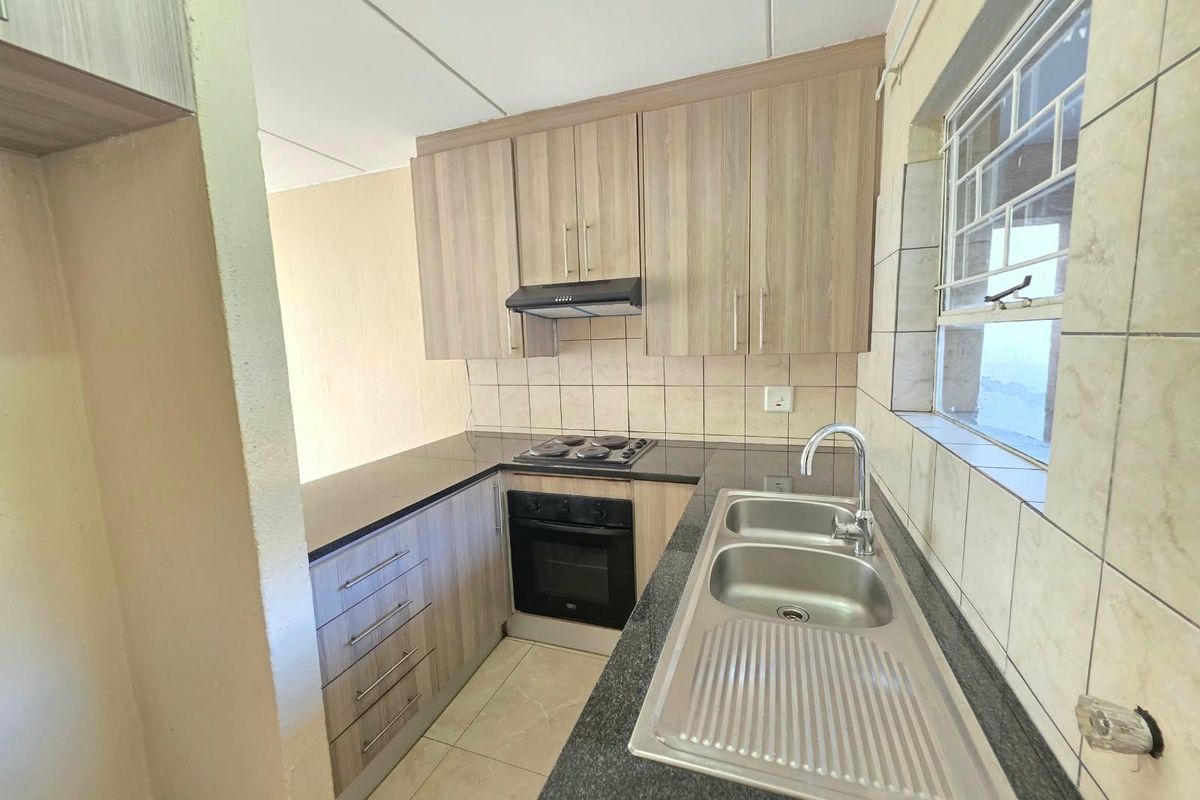 A functional kitchen featuring wood-look cabinetry, dark laminate countertops, a stainless steel sink, and built-in electric cooking appliances.