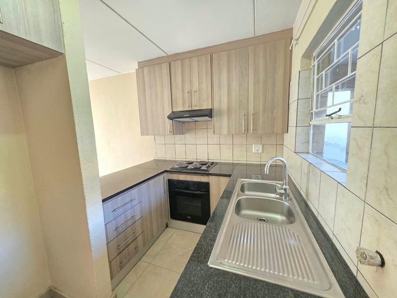 A functional kitchen featuring wood-look cabinetry, dark laminate countertops, a stainless steel sink, and built-in electric cooking appliances.