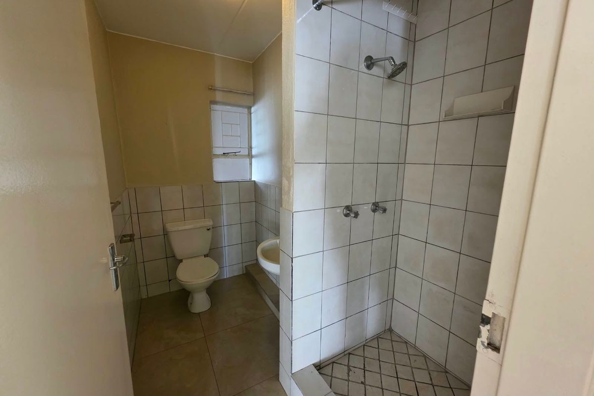 A functional bathroom featuring a shower enclosure, pedestal basin, and toilet with tiled finishes, requiring some maintenance and cosmetic updates.