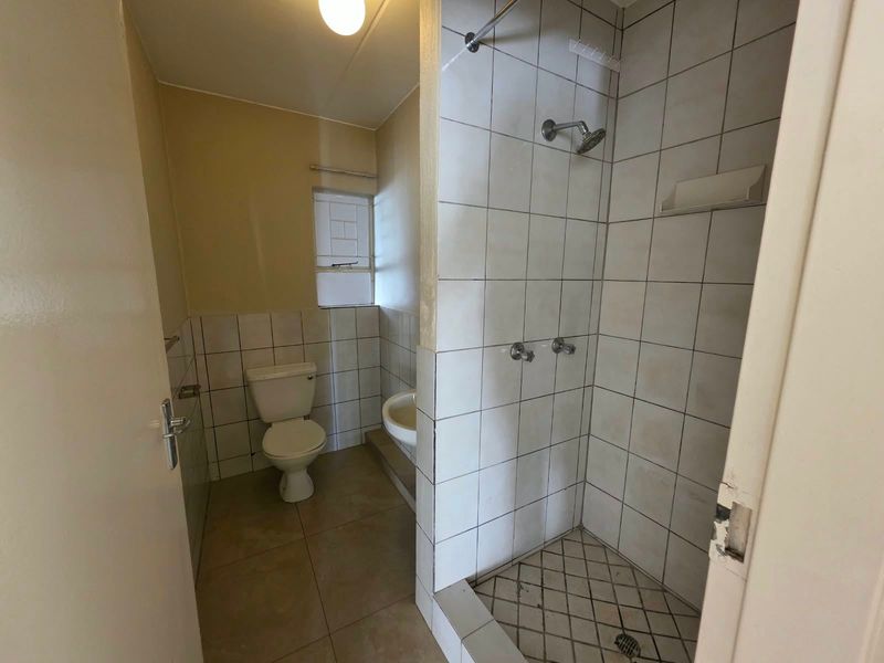 A functional bathroom featuring a shower enclosure, pedestal basin, and toilet with tiled finishes, requiring some maintenance and cosmetic updates.