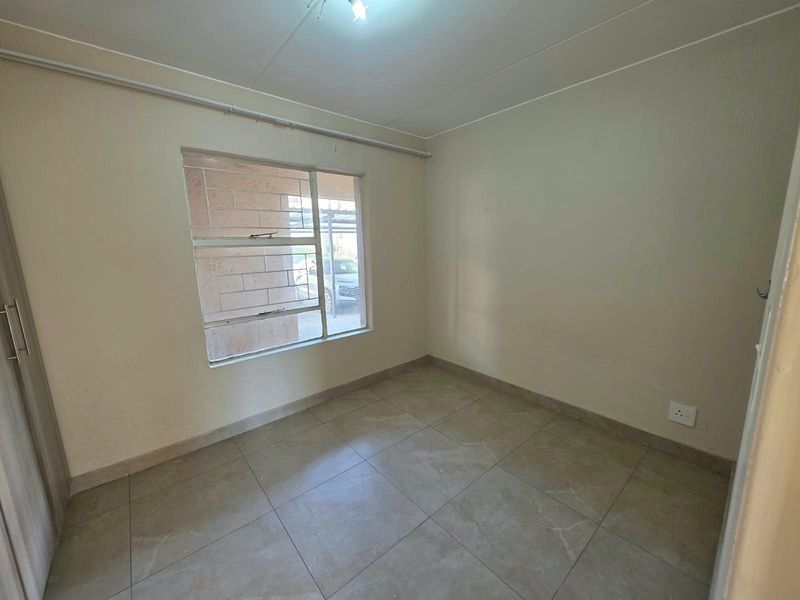 An empty bedroom featuring tiled flooring, a built-in cupboard, and an aluminium window frame, offering a neutral space ready for personalization.