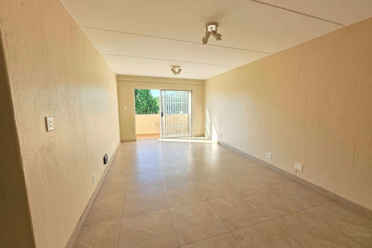 An empty, neutrally painted living area featuring tiled flooring and a sliding glass door leading to an outdoor balcony.