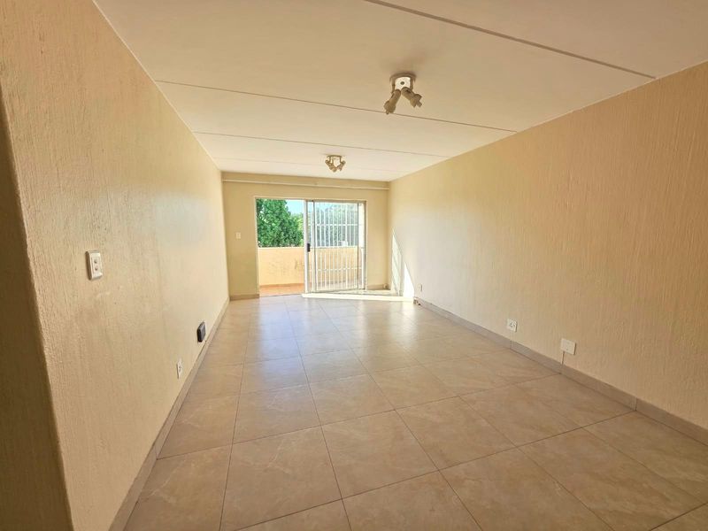 An empty, neutrally painted living area featuring tiled flooring and a sliding glass door leading to an outdoor balcony.