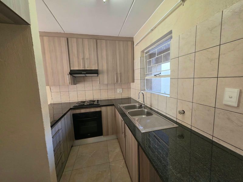 A compact kitchen featuring wood-finish cabinetry, granite countertops, a double basin sink, and built-in cooking appliances with tiled finishes throughout.