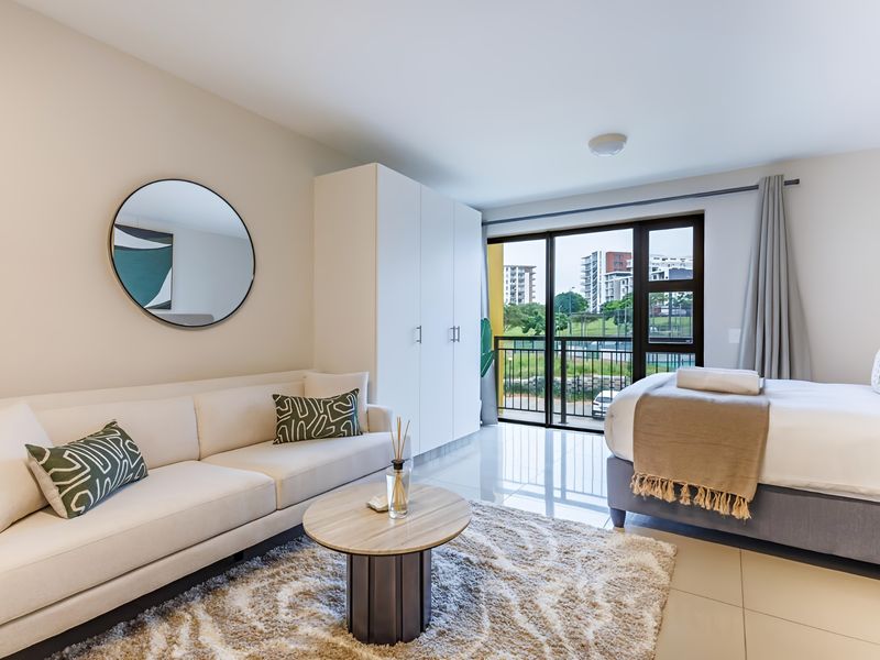 Modern open-plan studio apartment featuring tiled floors, a built-in wardrobe, and large sliding glass doors leading to a private balcony with scenic views.