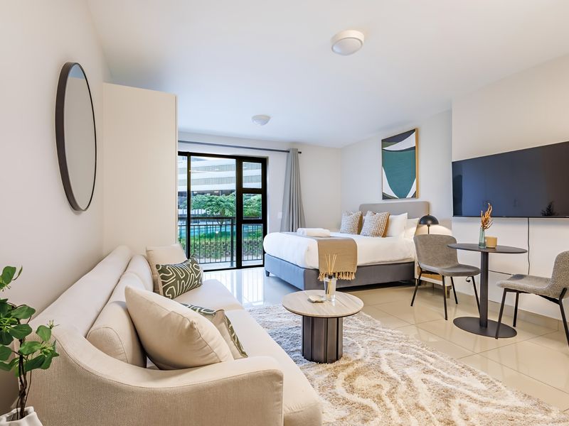 A well-maintained open-plan studio apartment featuring tiled flooring, modern recessed lighting, and a sliding glass door leading to a private balcony.