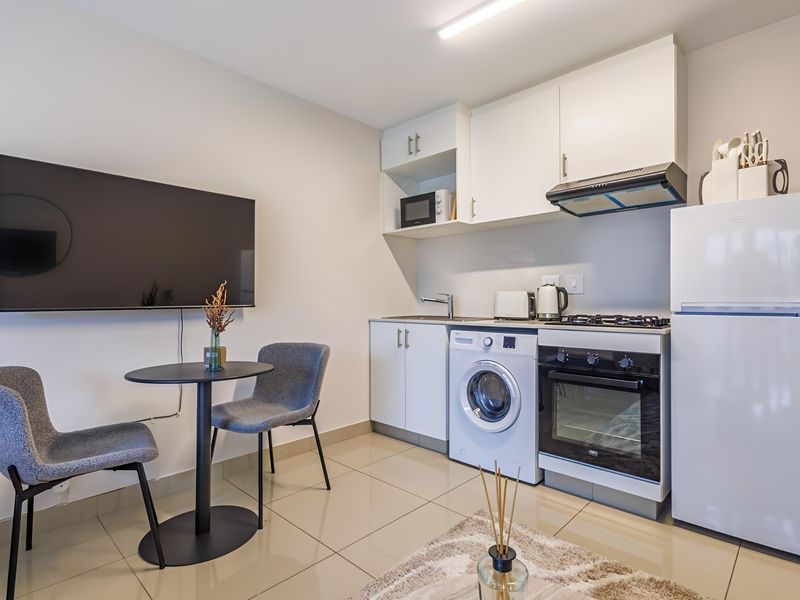 Compact open-plan kitchen area featuring modern white cabinetry, built-in oven, gas hob, extractor fan, and tiled flooring in a well-maintained apartment setting.