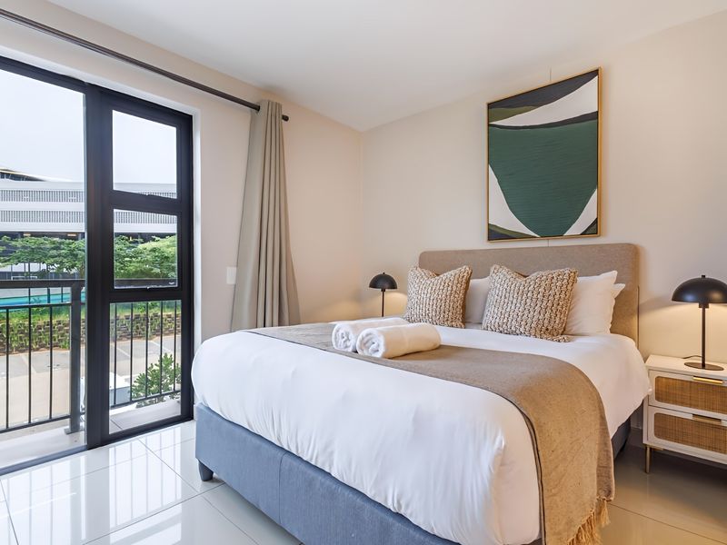 A modern, well-maintained bedroom featuring tiled flooring and a large sliding glass door providing access to a private balcony.