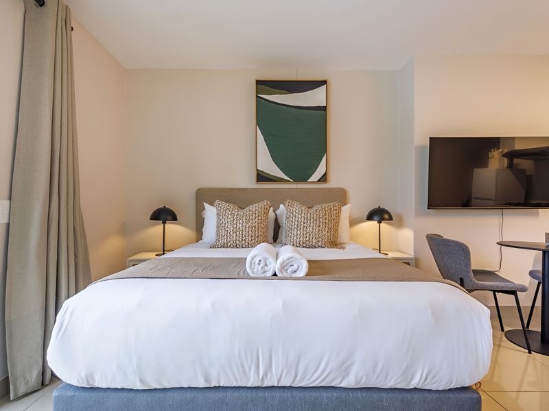 A well-maintained bedroom featuring neutral wall tones, tiled flooring, and integrated curtain tracks, offering a clean and comfortable living space.