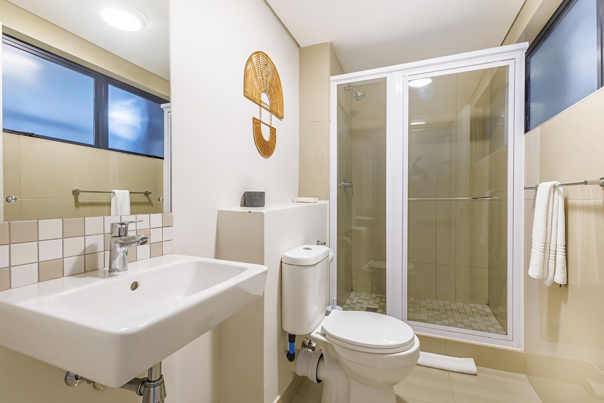 A clean and modern bathroom featuring a glass-enclosed shower, wall-mounted basin, and neutral tiled finishes throughout.