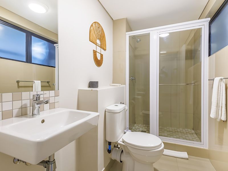 A clean and modern bathroom featuring a glass-enclosed shower, wall-mounted basin, and neutral tiled finishes throughout.