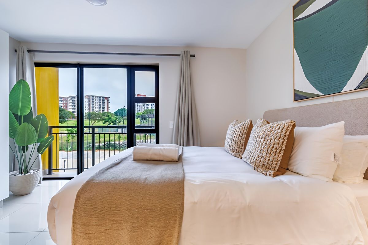 A bright and modern bedroom featuring tiled floors and a large sliding glass door that opens onto a private balcony with exterior views.