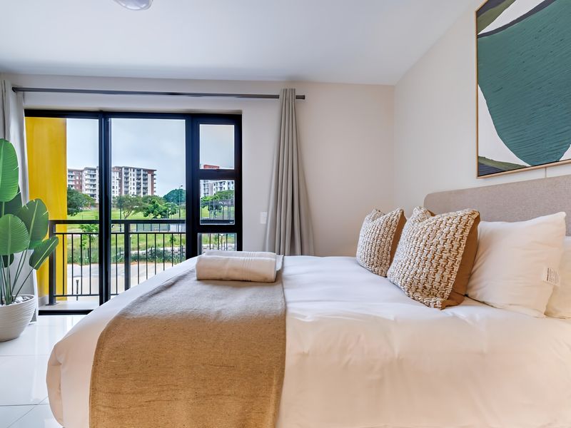 A bright and modern bedroom featuring tiled floors and a large sliding glass door that opens onto a private balcony with exterior views.