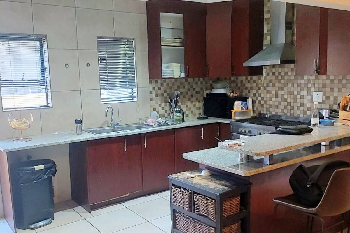 A functional kitchen featuring dark wood cabinetry, granite countertops, a breakfast bar, and a tiled backsplash with integrated gas hob and extractor fan.