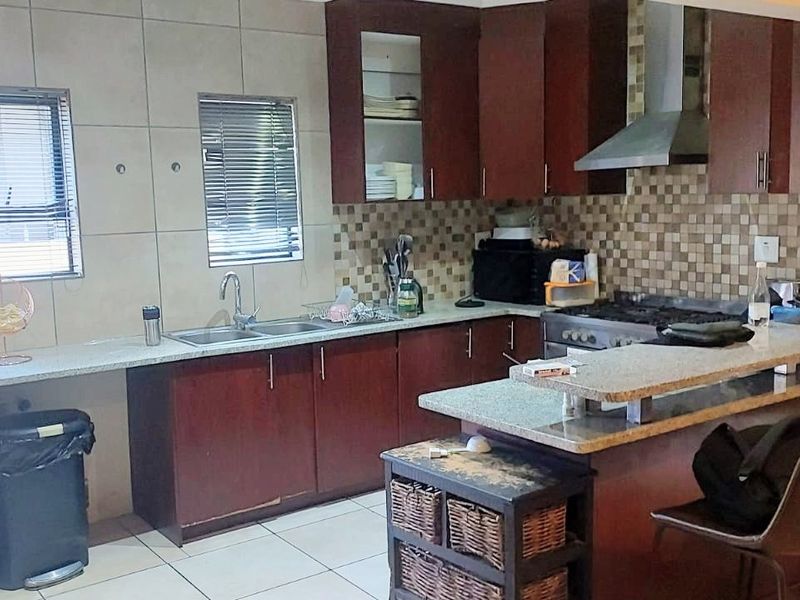 A functional kitchen featuring dark wood cabinetry, granite countertops, a breakfast bar, and a tiled backsplash with integrated gas hob and extractor fan.
